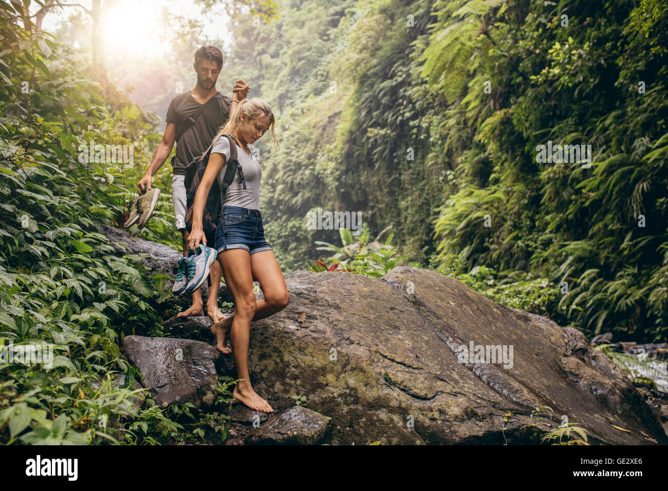 Shot of young couple walking through the mountain trail. Man and woman hiking on mountain trail barefoot. Stock Photo