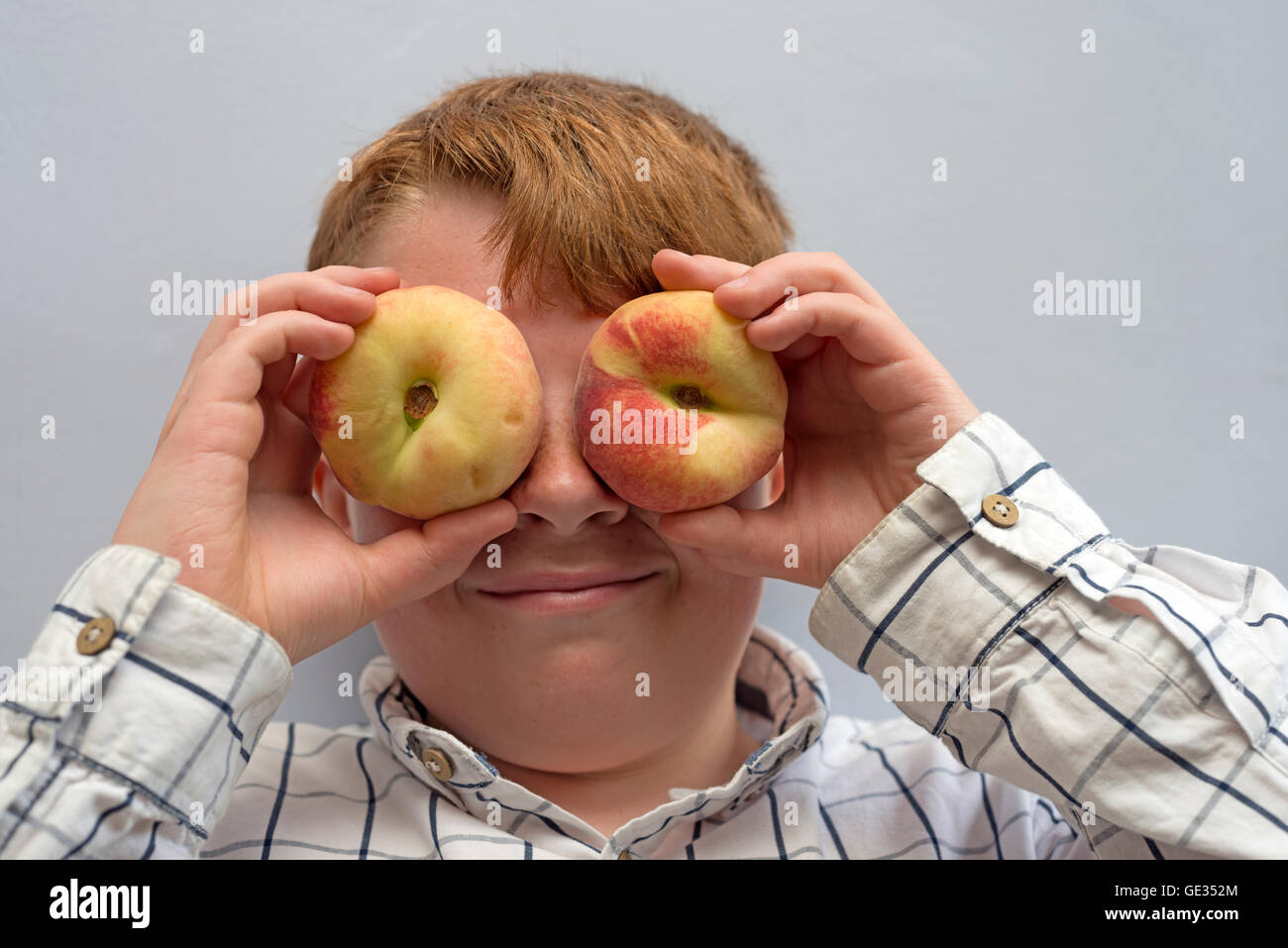 Ginger haired boy holding fresh peaches to his eyes Stock Photo