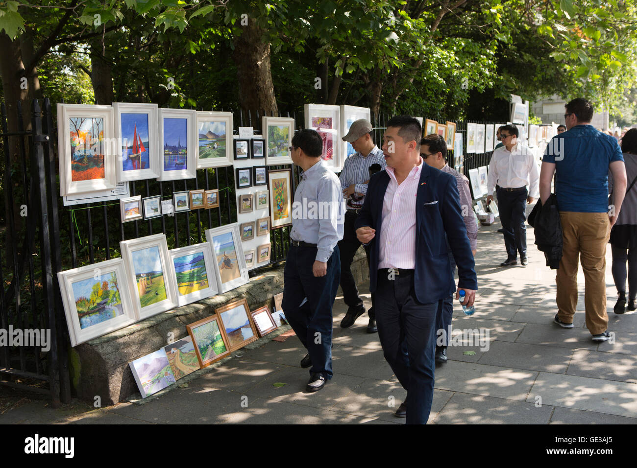 Ireland, Dublin, Merrion Square West, Sunday art market, Chinese tourists looking at paintings hanging on railings Stock Photo