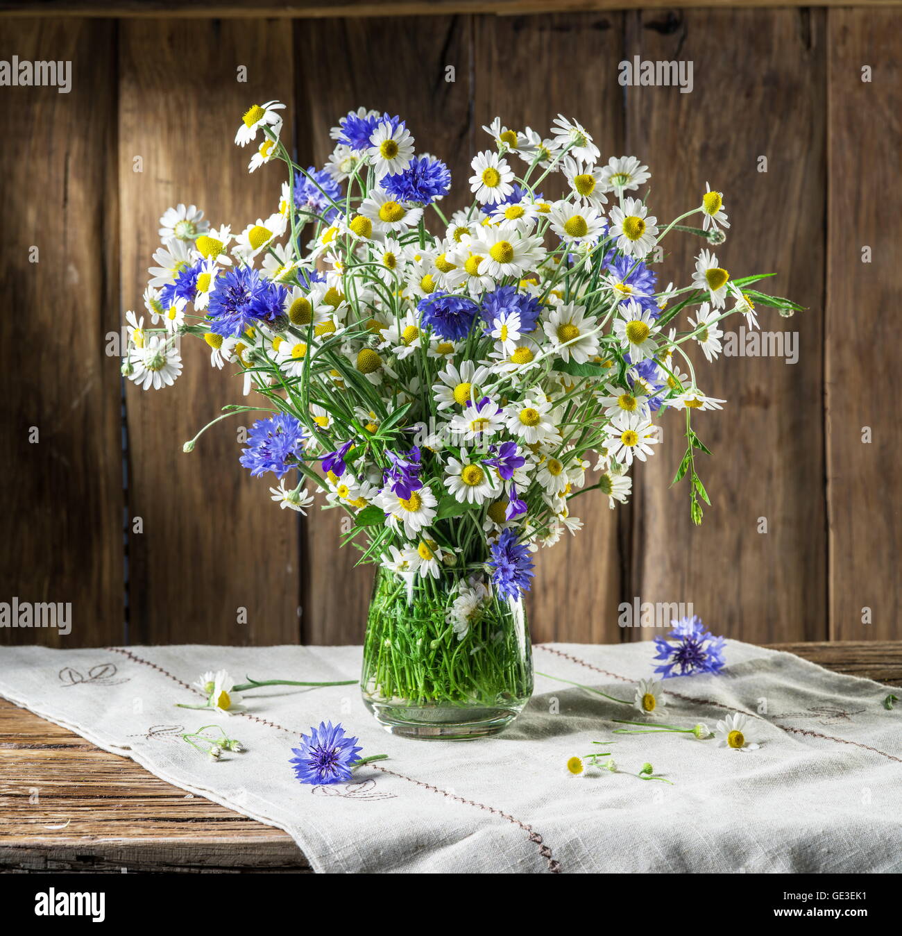 Bouquet of chamomiles and cornflowers in the vase on the wooden table ...