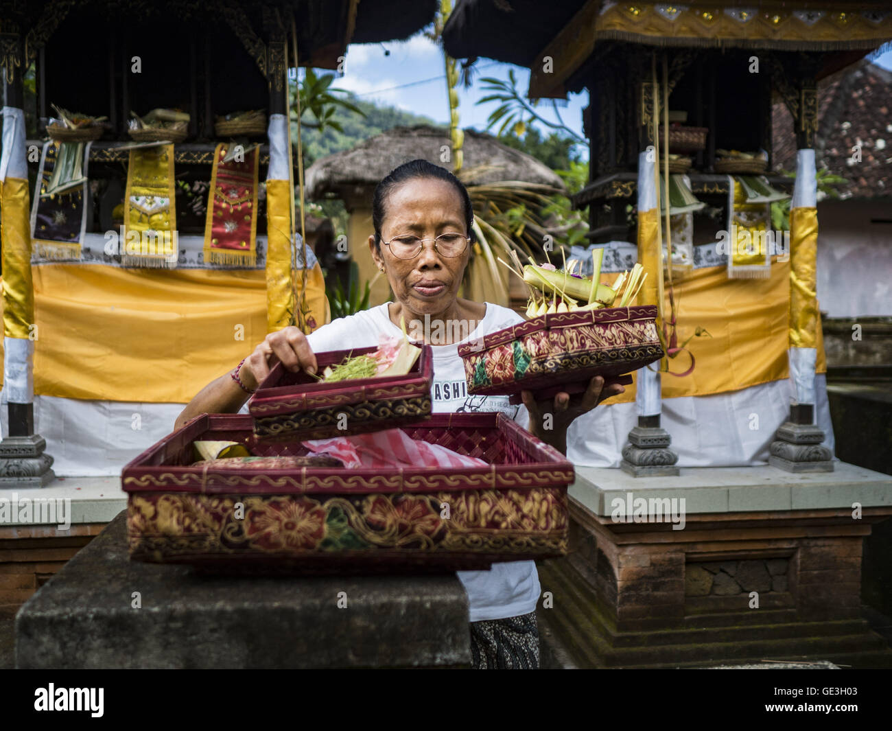 July 22, 2016 - Tenganan Duah Tukad, Bali, Indonesia - A woman makes an offering in her family temple in the Tenganan Duah Tukad village on Bali before the Pandanus fights. The ritual Pandanus fights are dedicated to Hindu Lord Indra. Men engage in ritual combat with spiky pandanus leaves and rattan shields. They usually end up leaving bloody scratches on the combatants' backs. The young girls from the community wear their best outfits to watch the fights. The fights have been traced to traditional Balinese beliefs from the 14th century CE. The fights are annual events in the Balinese year, wh Stock Photo