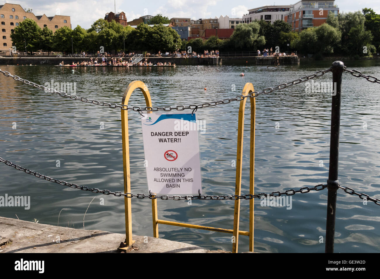 A 'Danger Deep Water, absolutely no swimming allowed' sign as people enjoy the cold water during hot sunny weather at Shadwell Basin in east London this afternoon. People have been warned not to swim in Shadwell Basin after a man drowned and died this week. Credit:  Vickie Flores/Alamy Live News Stock Photo