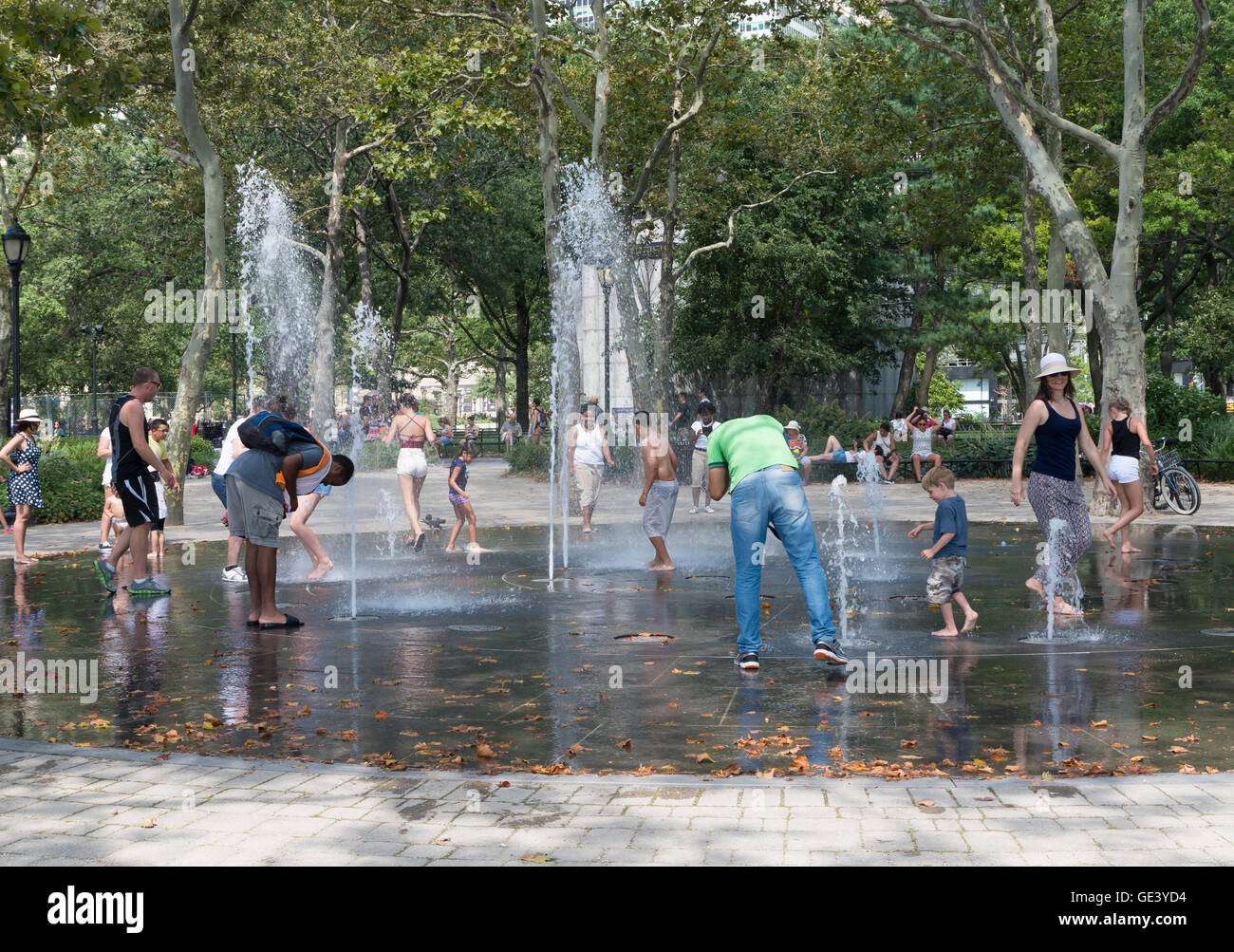 Adults and children play in water fountains in Battery Park, New York, to cool off during a heat wave. Stock Photo