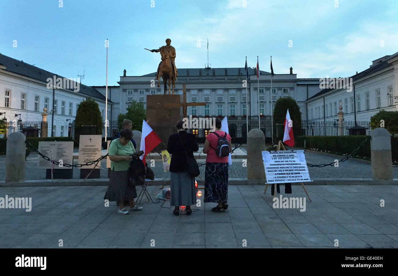 Warsaw, Poland. 12th July, 2016. Supporters of the national-conservative Law and Justice (PiS) party have errected a wooden cross outside the presidential palace in Warsaw, Poland, 12 July 2016. The sign the three women and one man have set up, in order not to be disturbed while praying, reads "we pray for Poland and the truth about 10.04.2010". PHOTO: NATALIE SKRZYPCZAK DPA/Alamy Live News Stock Photo
