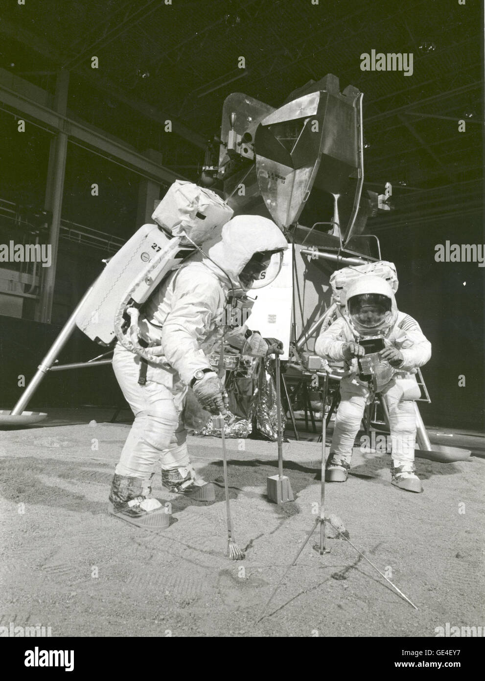 The Apollo 11 crew simulates deploying and using lunar tools on the surface of the Moon during a training exercise on April 22, 1969. Astronaut Buzz (Aldrin Jr. on left), lunar module pilot, uses a scoop and tongs to pick up a soil sample. Astronaut Neil A. Armstrong, Apollo 11 commander, holds a bag to receive the sample. In the background is a Lunar Module mockup.  Image # : S-69-32233  Date: April 22, 1969 Stock Photo