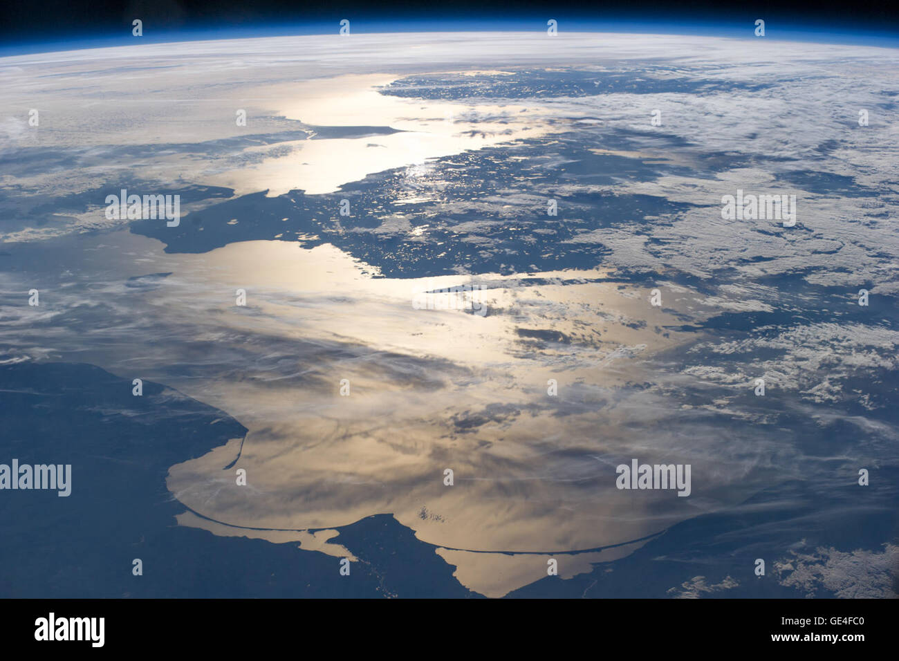 Description An astronaut on the International Space Station (ISS) took this panorama looking aft of the spacecraft (backwards along the orbital path) as the Sun was setting over the North Sea. Seen from the ISS, the Sun’s reflection point moves quickly across the landscape, momentarily lighting up water bodies. In this fleeting view from June 15, 2014, the coast of southern Norway is outlined near the horizon. The brightest reflection highlights the narrow sea passage known as the Skagerrak—revealing the thin tip of Denmark. Numerous small lakes in southern Sweden appear at image center, and s Stock Photo