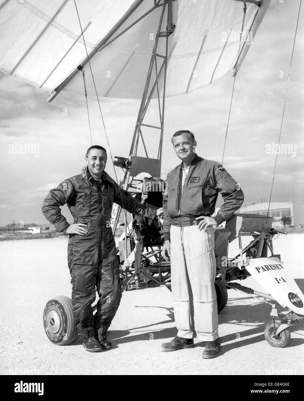 The Paresev 1-A standing at Rogers Dry Lakebed at the NASA Flight Research Center (now Armstrong Flight Research Center), Edwards, California. Mercury Astronaut Gus Grissom is at left and NASA test pilot Milton Thompson is at right. The Paresev evaluated a potential replacement for parachutes used on spacecraft. The Paresev was steerable and was evaluated for use on the Gemini spacecraft. The idea was not workable, however.  Image # : E-8937 Date: October 17, 1962 Stock Photo