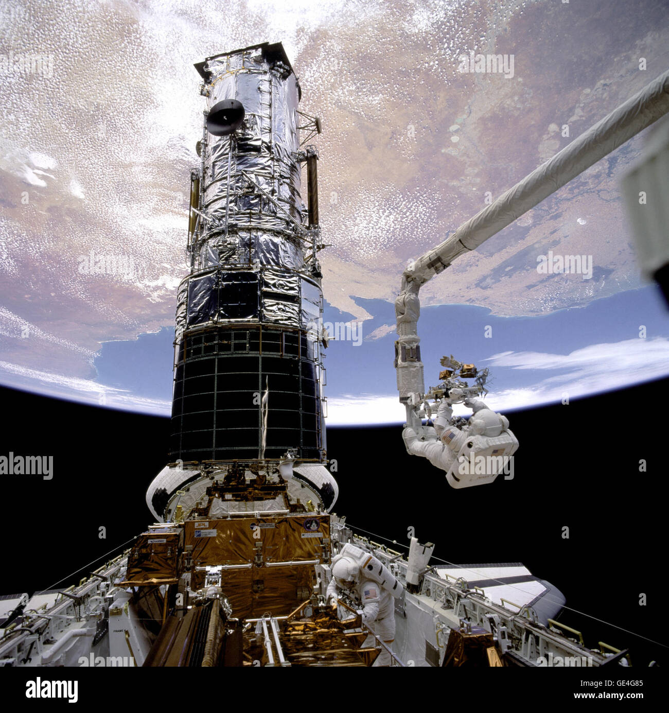 Astronaut F. Story Musgrave, anchored on the end of the Remote Manipulator  System (RMS) arm, prepares to be elevated to the top of the Hubble Space  Telescope (HST) to install protective covers