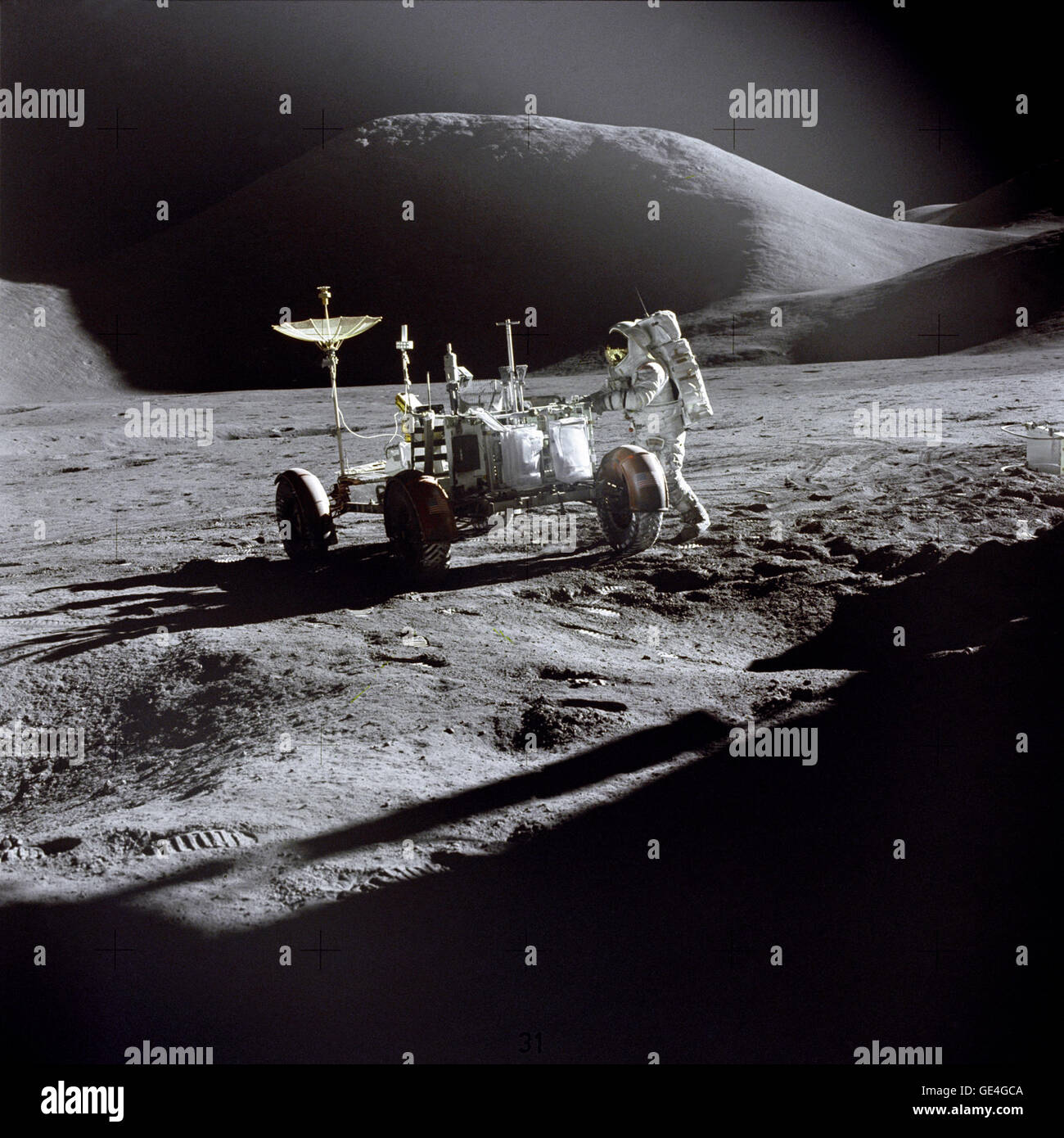 Astronaut James B. Irwin, Lunar Module pilot, works at the Lunar Roving Vehicle during the first Apollo 15 lunar surface extravehicular activity (EVA-1) at the Hadley-Apennine landing site. The shadow of the Lunar Module &quot;Falcon&quot; is in the foreground. This view is looking northeast, with Mount Hadley in the background. This photograph was taken by Astronaut David R. Scott, Commander.   Image # : AS15-86-11603 Stock Photo