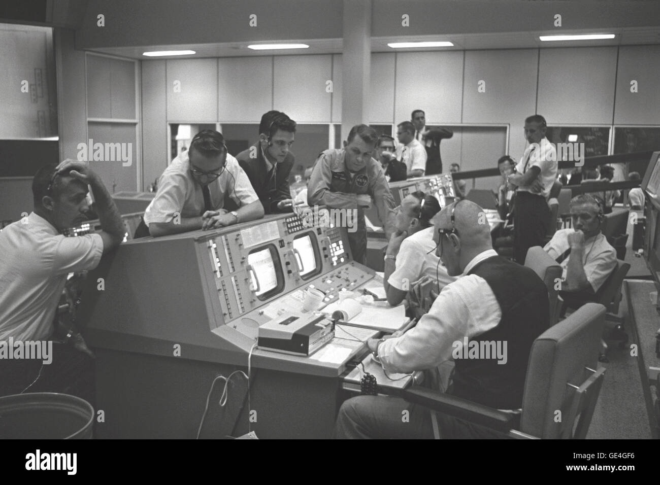 View of the Flight Directors console in the Mission Control Center (MCC), Houston, Texas, during the Gemini 5 flight. Seated at the console are Eugene F. Kranz (foreground) and Dr. Christopher C. Kraft Jr. (background). Standing in front of the console are Dr. Charles Berry (left), an unidentified man in the center and astronaut Elliot M. See.  Image # : S65-28689 Stock Photo