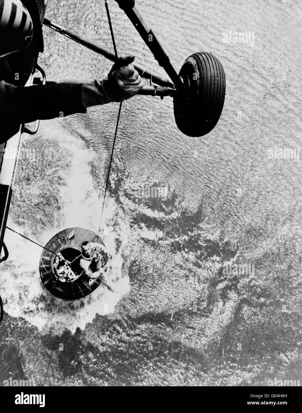 Astronaut Alan B. Shepard Jr., pilot of the Mercury-Redstone 3 (MR-3) suborbital spaceflight, is retrieved by a helicopter from the USS Lake Champlain during recovery operations in the western Atlantic Ocean. Shepard and the Mercury spacecraft designated the &quot;Freedom 7&quot; (floating in water below) were flown to the deck of the recovery ship within 11 minutes of splashdown. MR-3 was the first American human space mission. The spacecraft attained a maximum speed of 5,180 miles per hour, reached an altitude of 116 1/2 statute miles, and landed 302 statute miles downrange from Cape Canaver Stock Photo