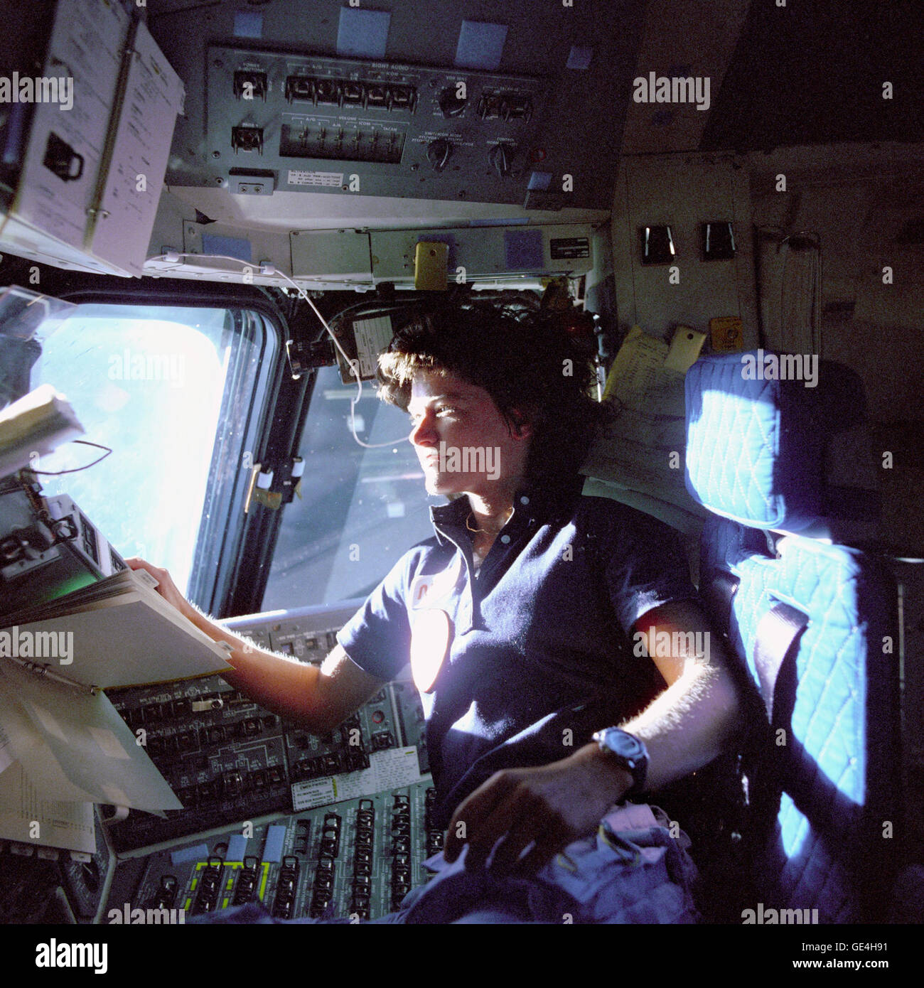 (June 1983) Astronaut Sally K. Ride, mission specialist on STS-7, monitors control panels from the pilot's chair on the Flight Deck. Floating in front of her is a flight procedures notebook.  Image # : S83-35783 Stock Photo