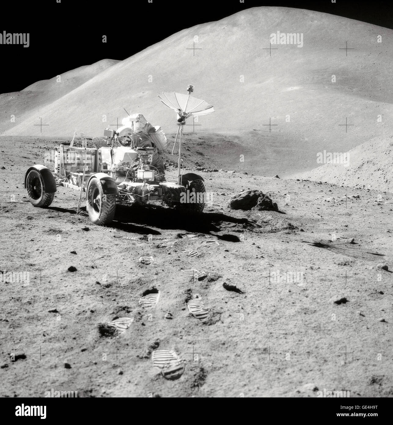 David R. Scott, Commander of Apollo 15, works at the Lunar Roving Vehicle (LRV) during the third lunar surface extravehicular activity (EVA) of the mission at the Hadley-Apennine landing site. Hadley Rille is at the right center of the picture. Hadley Delta, in the background, rises approximately 4,000 meters (about 13,124 feet) above the plain. St. George Crater is partially visible at the upper right edge. This photograph was taken by Lunar Module pilot James B. Irwin. This view is looking almost due South.   Image # : AS15-82-11121 Stock Photo