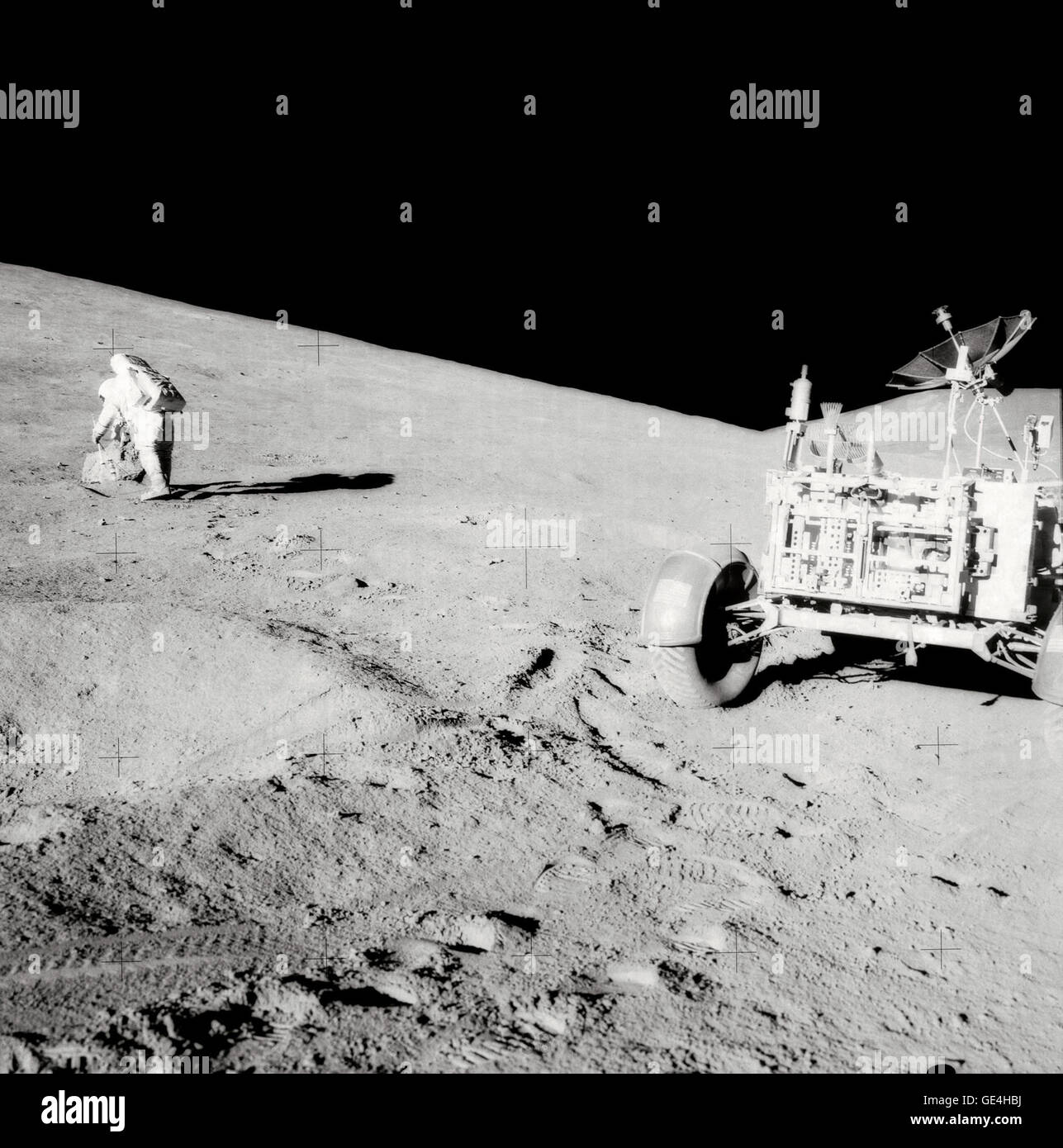 Astronaut David R. Scott, mission commander, with tongs and gnomon in hand, studies a boulder on the slope of Hadley Delta during the Apollo 15 lunar surface extravehicular activity. The Lunar Roving Vehicle (LRV) or Rover is in right foreground. View is looking slightly south of west. &quot;Bennett Hill&quot; is at extreme right. Astronaut James B. Irwin, lunar module pilot, took this photograph.   Image # : AS15-85-11437 Date: August 1, 1971 Stock Photo