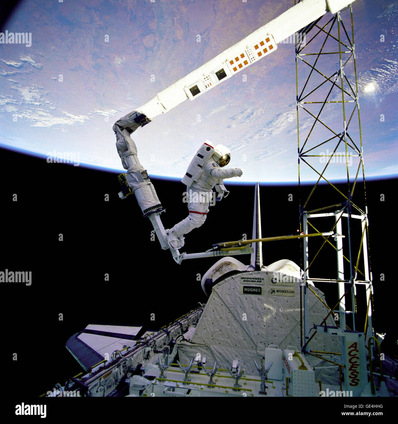 Astronaut Jerry L. Ross, anchored to the foot restraint on the Remote Manipulator System (RMS), approaches the tower-like Assembly Concept for Construction of Erectable Space Structures (ACCESS) device. The structure was just deployed by Ross and astronaut Sherwood Spring as the Atlantis flies over white clouds and blue ocean waters of the Atlantic.  Image # : 61B-41-019  Date: December 1, 1985 Stock Photo