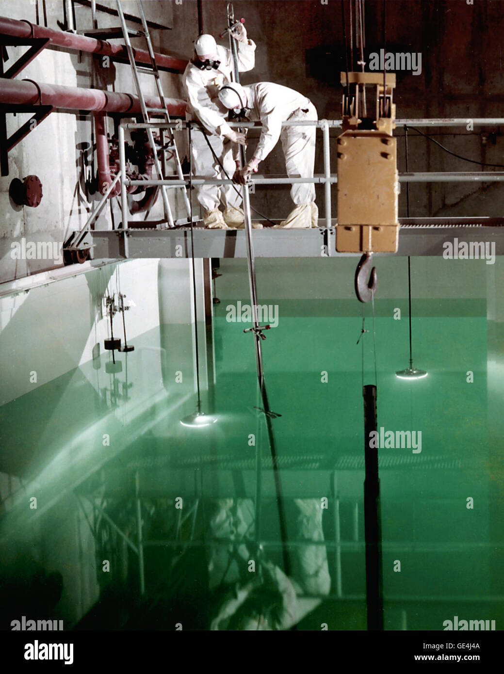 Two technicians clad in anti-contamination clothing manipulate a shim safety control rod in a water canal in the hot laboratory. The twenty- five foot deep water provided shielding from the radiation, yet still enabled visible contact with the research experiments. The water also allowed the underwater transfer of irradiated materials from the reactor to the hot laboratory for inspection. Moving materials by canal reduced the need for lead transfer casks, though they were still needed when the radioactive materials were taken out of the water.  Image # : C-1961-55808 Stock Photo