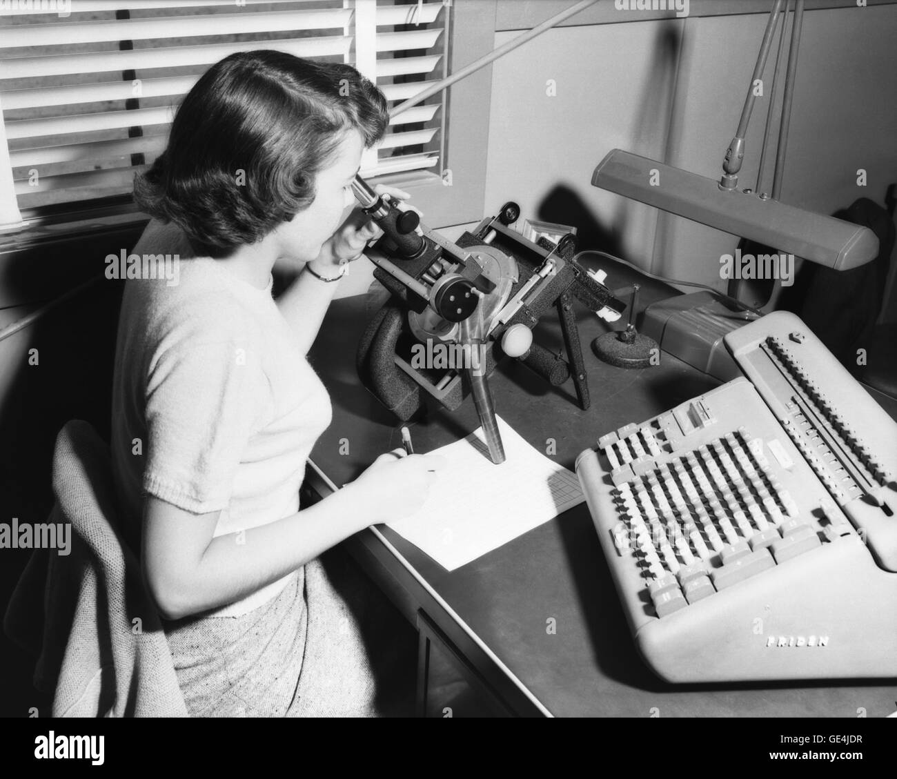 A human computer at work with a microscope collecting data at Langley Research Center.  She sits next to a Friden calculating machine.  The National Advisory Committee for Aeronautics (NACA) hired women to serve as &quot;computers&quot; in the mid 1930s, doing the drudge work of reading data from test results (from film as shown here), calculating formulas and plotting results.    Image # : L-74768  Date: March 24, 1952 Stock Photo