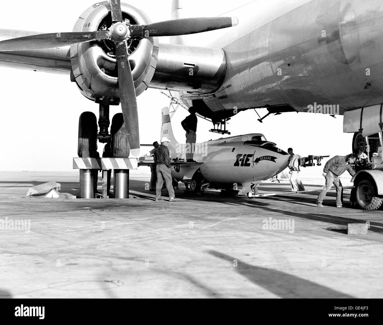 In 1955, the Bell X-1E rocket plane is loaded under the Boeing B-29 for high-speed flight testing. This image captures the process at the NACA High-Speed Flight Research Station. The X-1E was part of a series of experimental aircraft used to advance aeronautical research during the early stages of the space race. Stock Photo