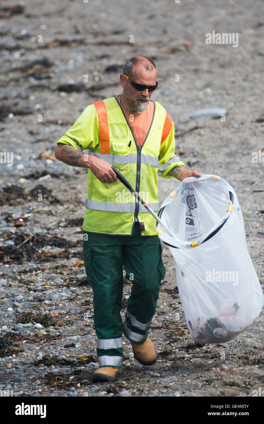 A man, employed by Ceredigion County Council local authority,  working as a litter picker cleaning rubbish trash and plastic waste off the the beach in Aberystwyth Wales UK Stock Photo