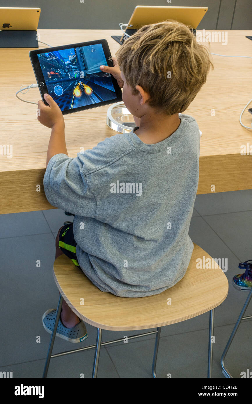 A young boy 7-8 years old plays a game on an iPad at the Apple Store in Santa Barbara, California. Stock Photo