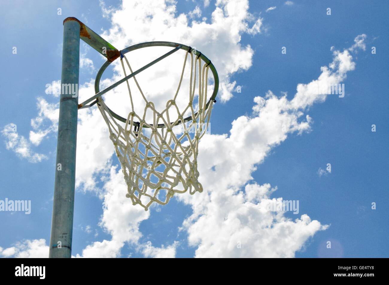 Abstract perspective of a netball rim with net against a blue sky and cloud background. Stock Photo