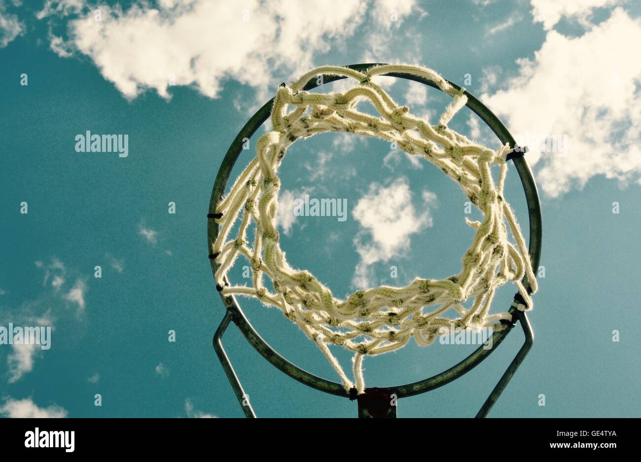 Abstract perspective of a netball rim with net against a blue sky and cloud background. Stock Photo