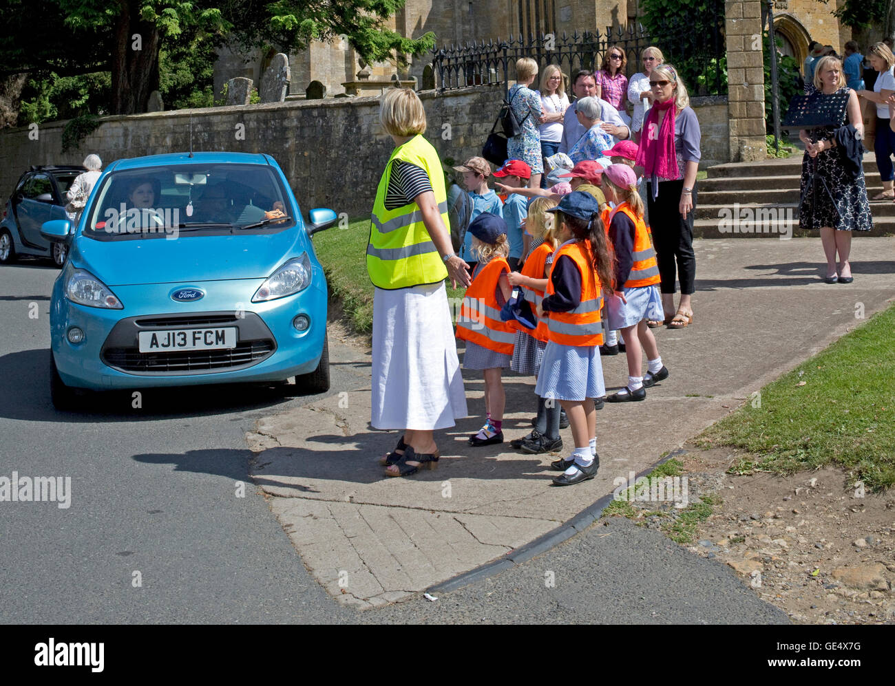 Teacher and children preparing to cross busy road Chipping Campden UK Stock Photo