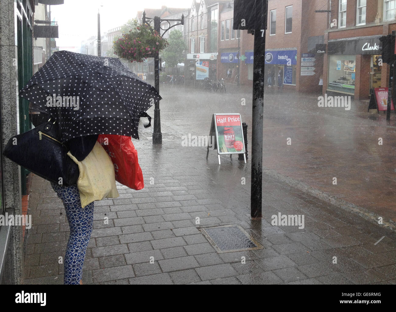 A woman trying to shelter herself and her shopping bags from torrential rain with a small umbrella in the town of Newbury, Berkshire, UK Stock Photo