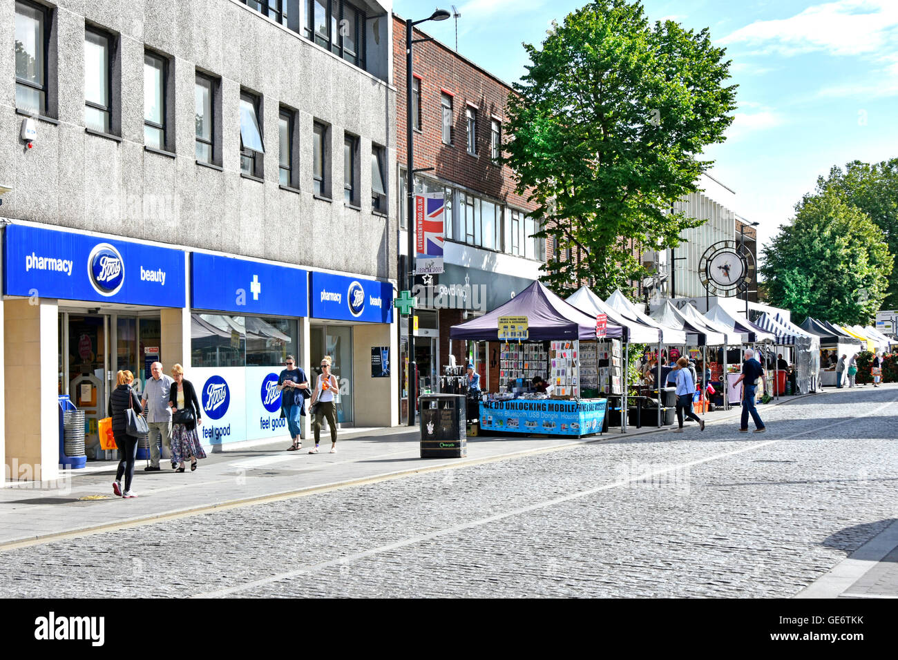 Street scene at Brentwood Essex England UK shopping High Street Boots pharmacy store and street market stalls beside cobblestone road Stock Photo