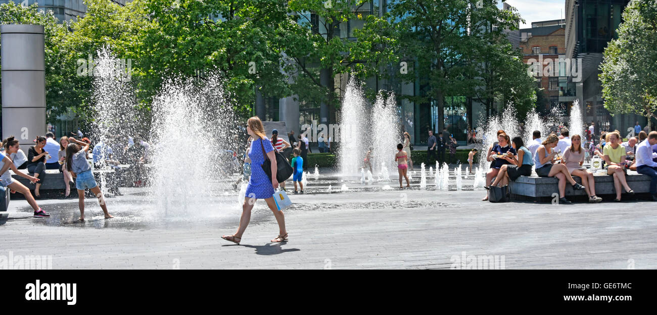 Water jets rising above block paving at random timings during hot London UK summer weather as office workers take lunch break & kids play in fountains Stock Photo
