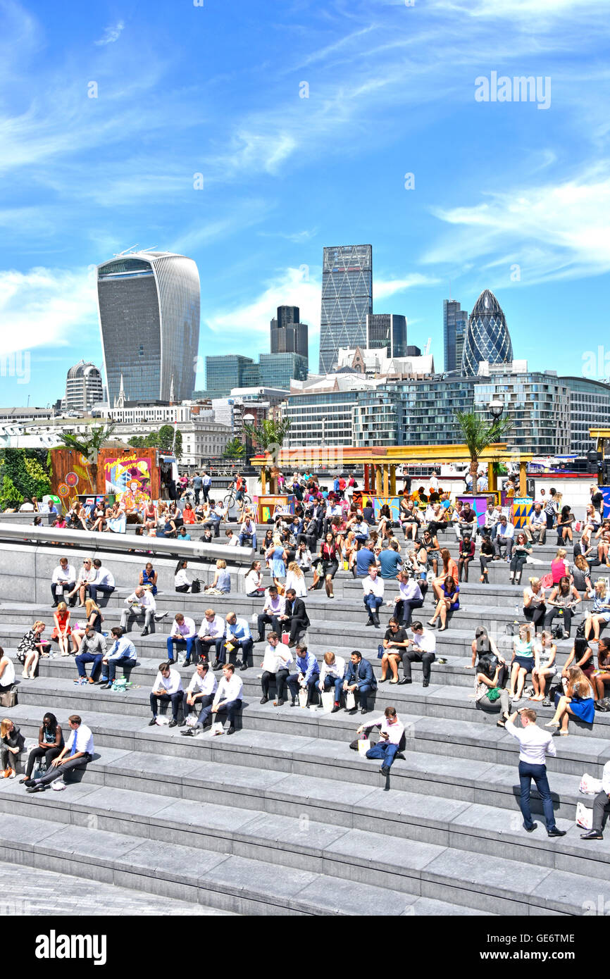 Southwark office workers taking hot sunny lunch break on steps at  More London Scoop riverside amphitheatre City Of London skyline beyond England UK Stock Photo