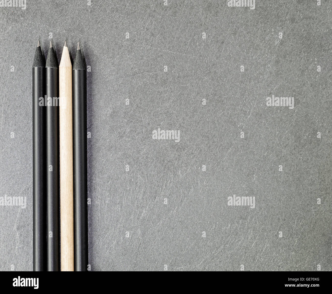 Light colored pencil among three black ones on a gray granite slate. Stock Photo