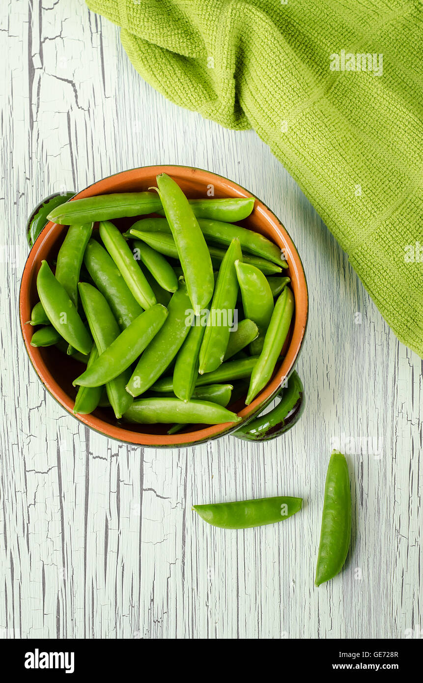 A bowl of fresh sugar snap peas and a kitchen towel on a white wooden table. Stock Photo