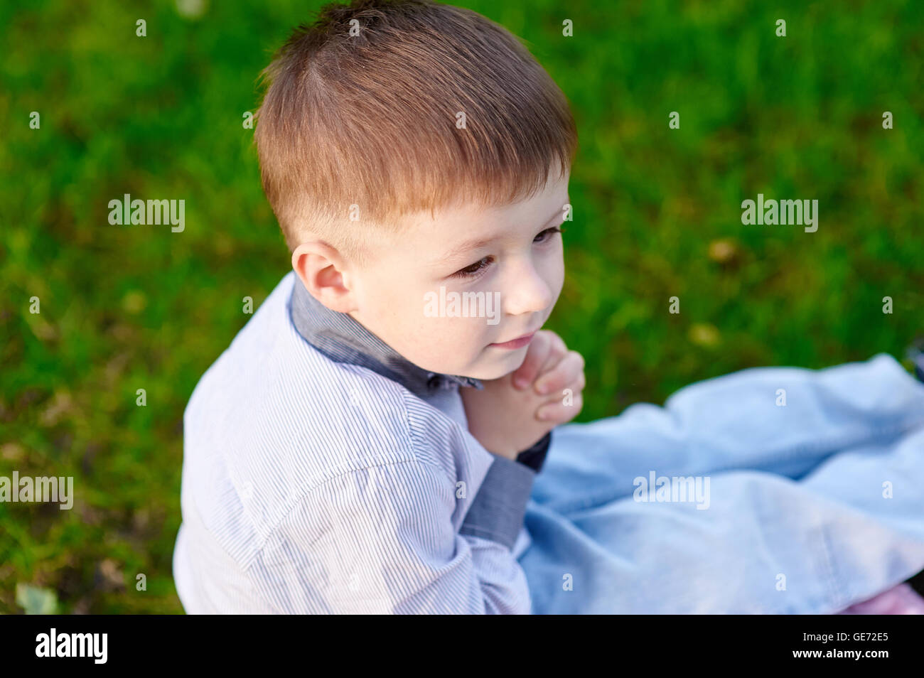 cheerful little boy sitting on the grass in the park Stock Photo