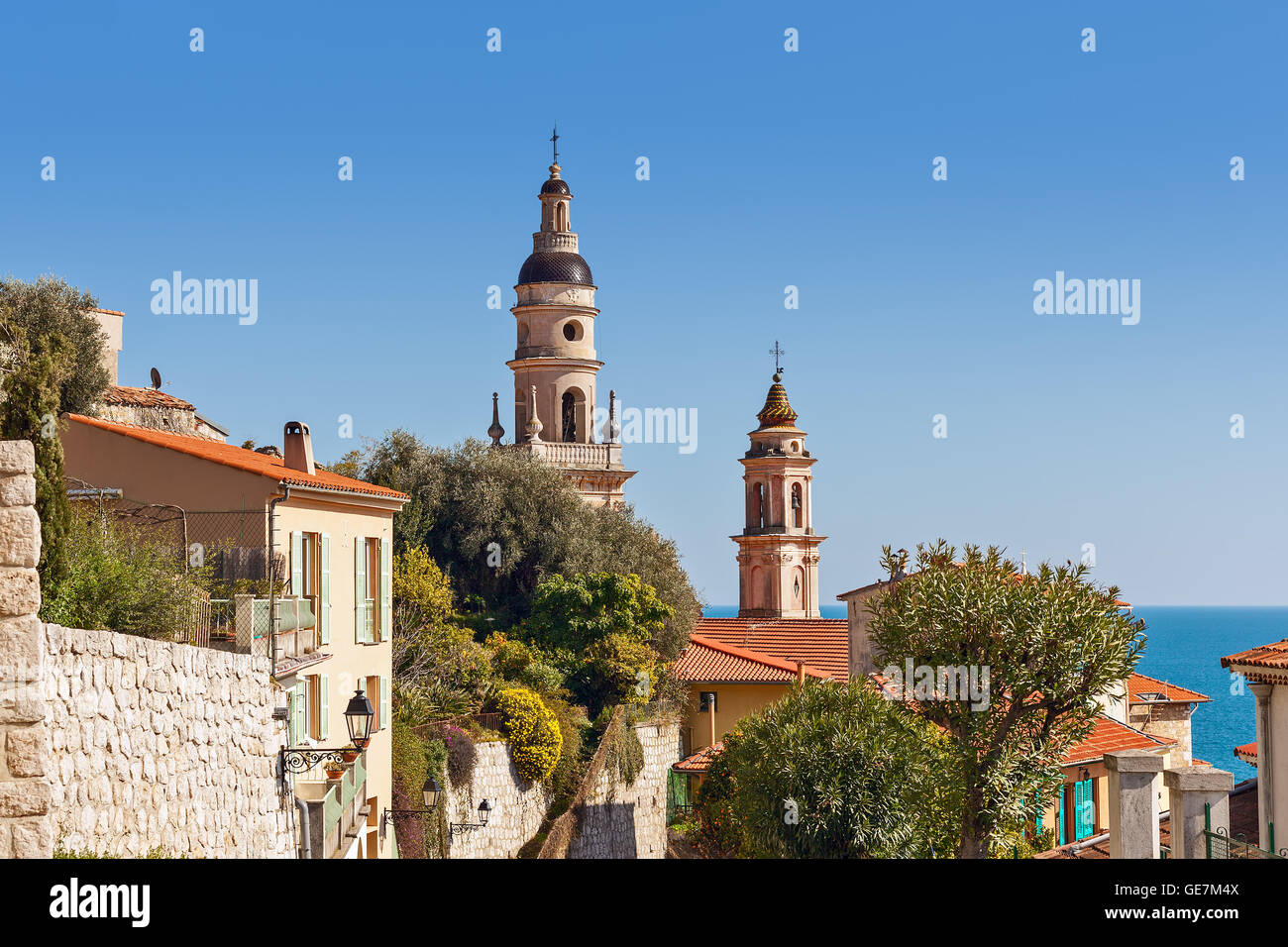 Two campaniles among houses under blue sky as Mediterranean sea on background in Menton, France. Stock Photo
