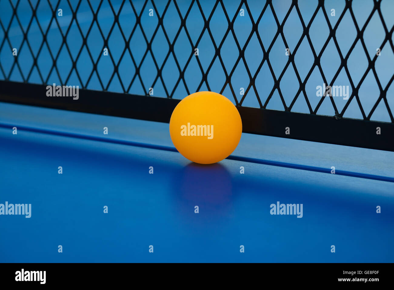 yellow ball hits the bottom of the net on a blue pingpong table close up Stock Photo