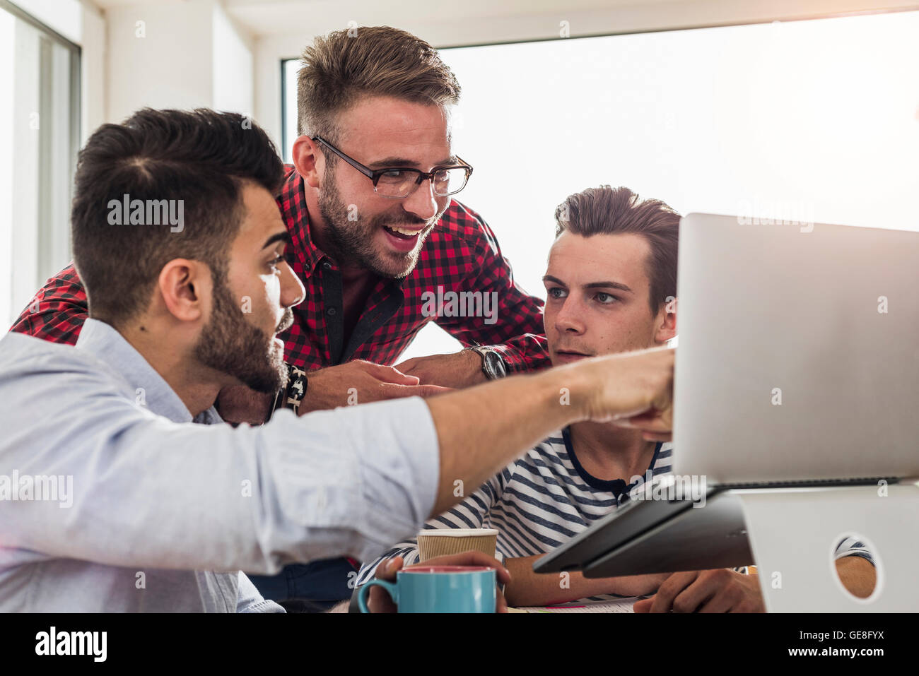 Three young professionals sharing laptop in office Stock Photo - Alamy