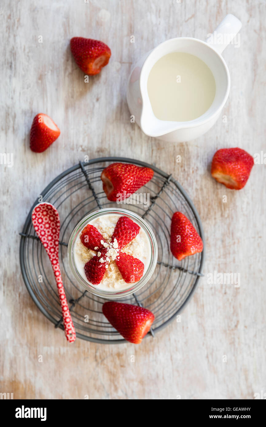Glass of overnight oats with strawberries and milk jug on wood Stock Photo