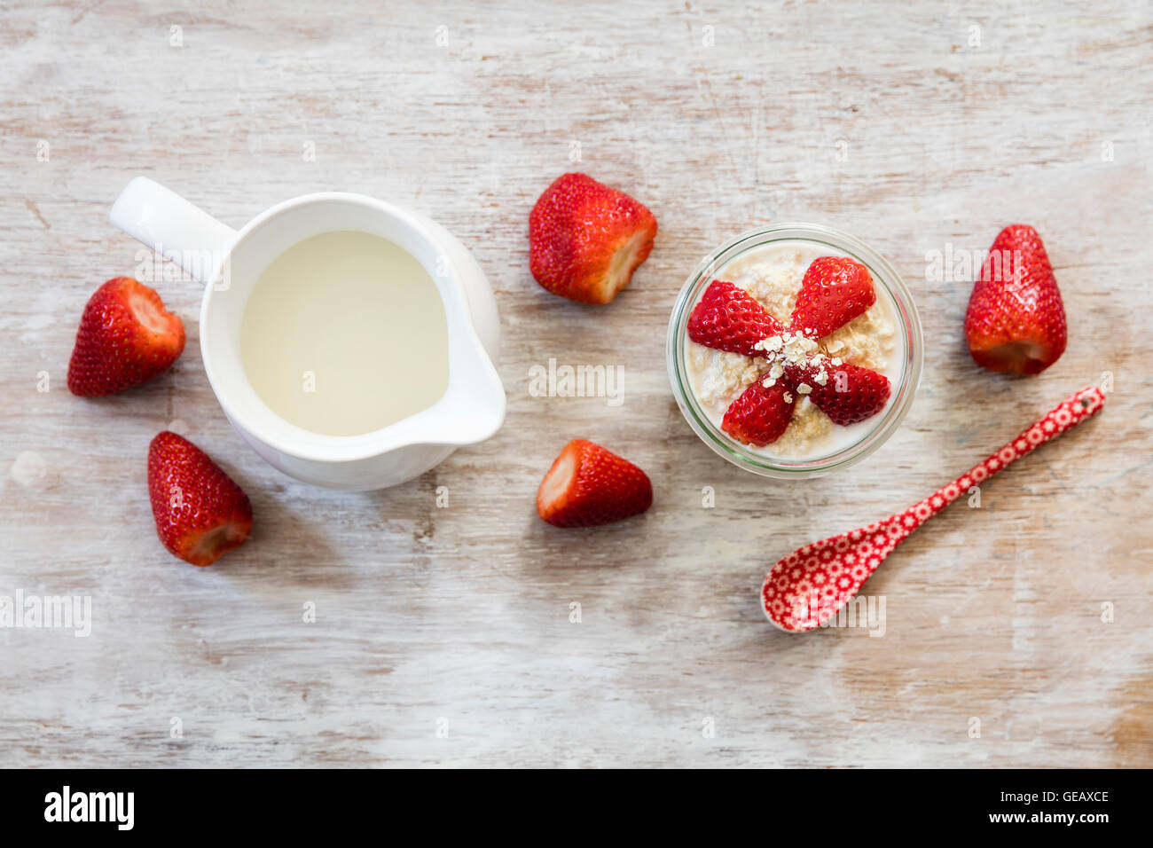 Glass of overnight oats with strawberries and milk jug on wood Stock Photo