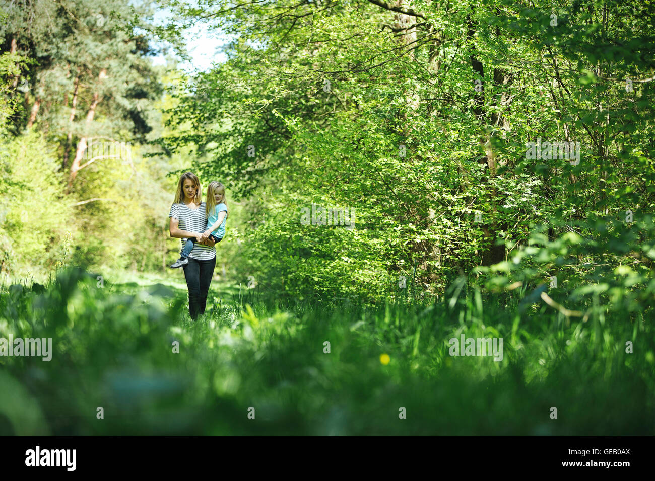 Mother carrying daughter in forest Stock Photo