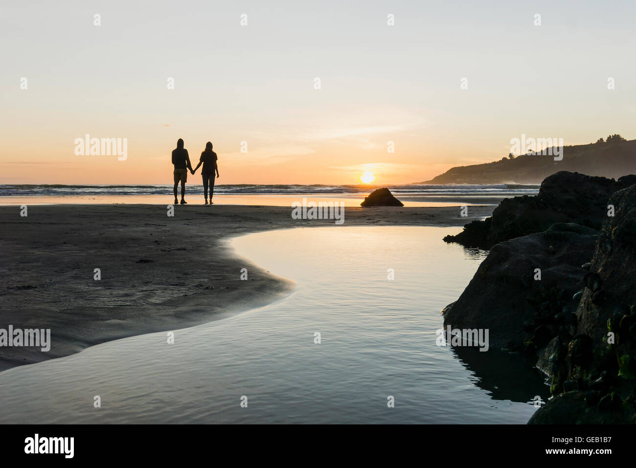 Silhouette of couple standing hand in hand on the beach looking at ...