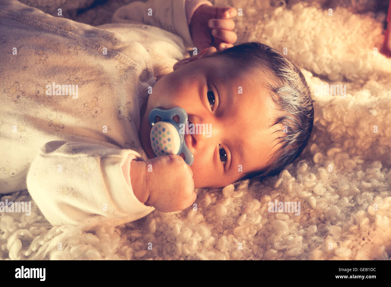 Afro european, baby just before falling asleep on a cozy white fur Stock Photo