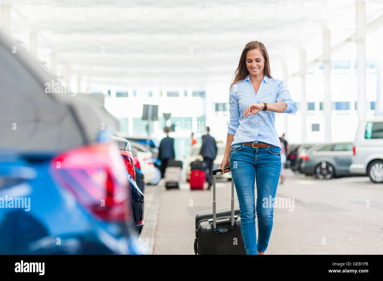 Smiling woman walking with luggage on parking lot Stock Photo