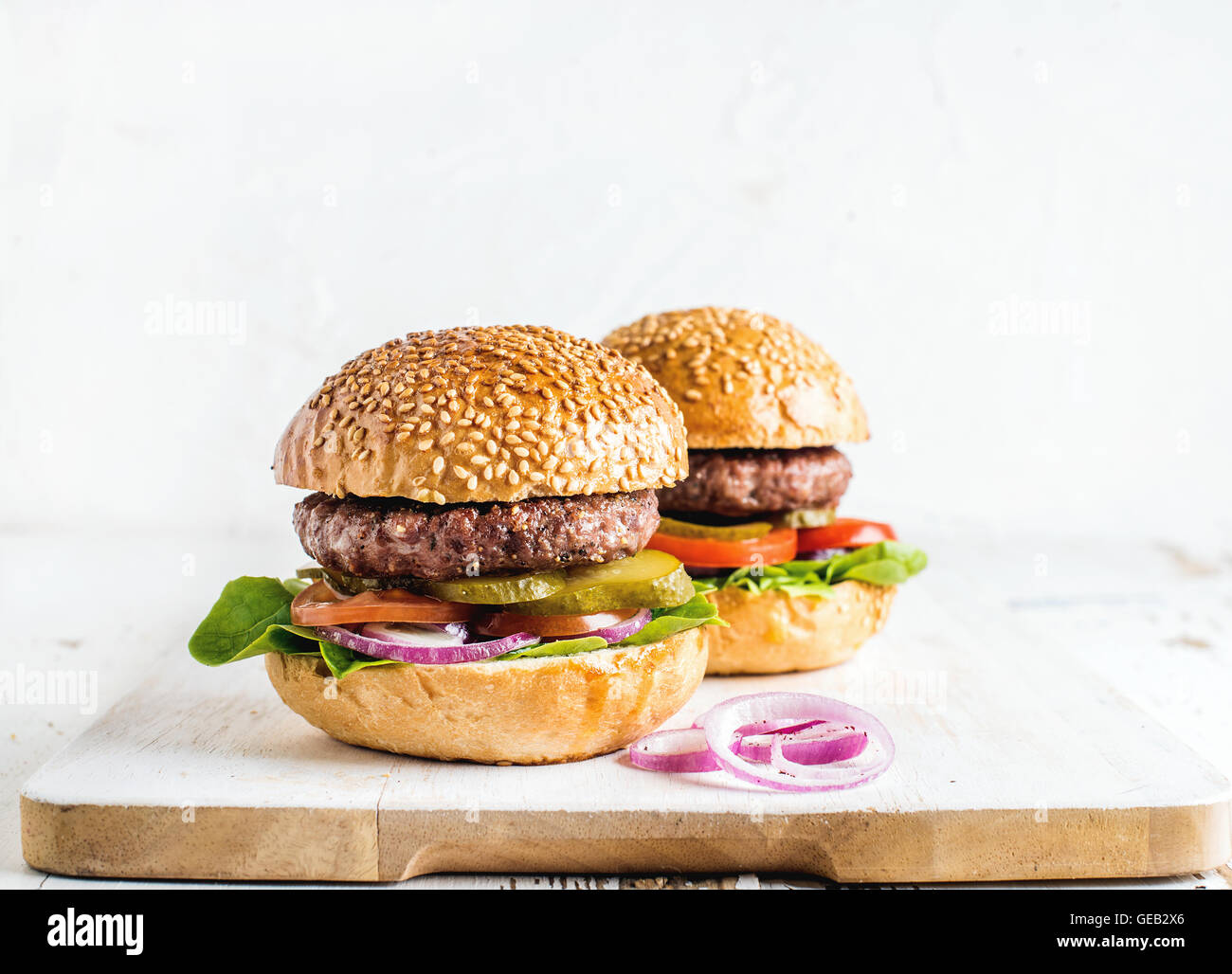 Fresh homemade burgers on wooden serving board with onion rings. Stock Photo