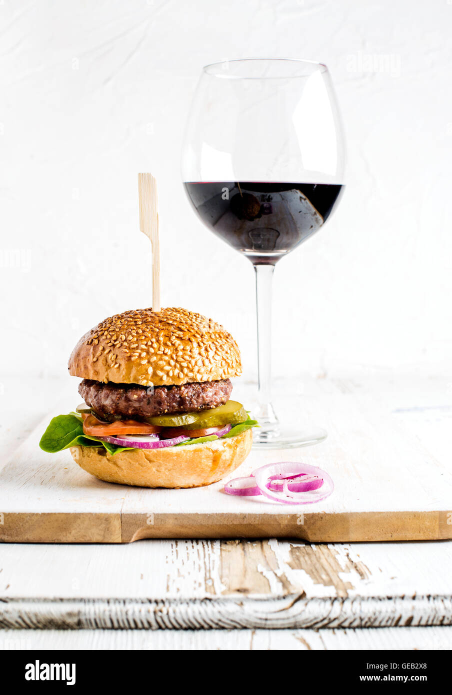 Fresh homemade burger on wooden serving board with onion rings and glass of red wine Stock Photo