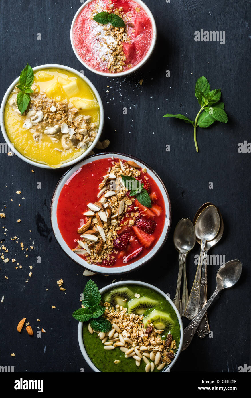 Healthy summer breakfast concept. Colorful fruit smoothie bowls with nuts and oat granola on black background Stock Photo