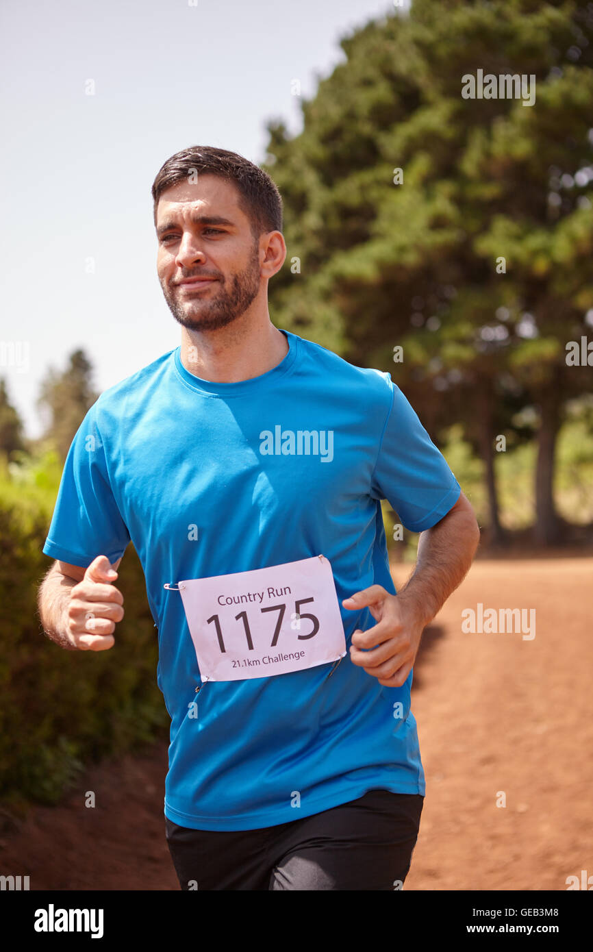 A young male running a cross country race with trees behind him