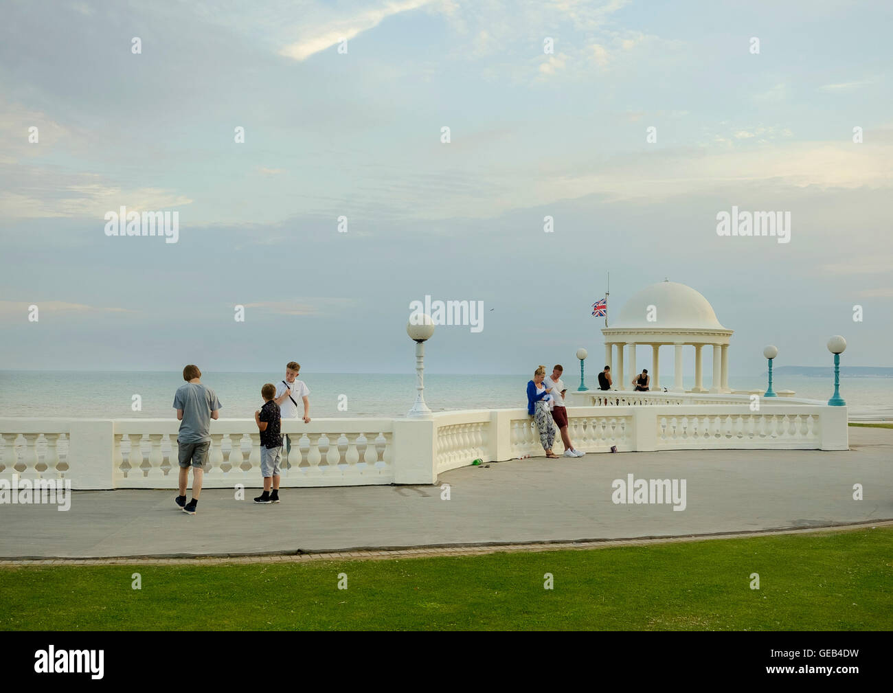 Young people congregating on a summer evening at the colonnade on the seafront at Bexhill-on-Sea, East Sussex, looking at their Stock Photo