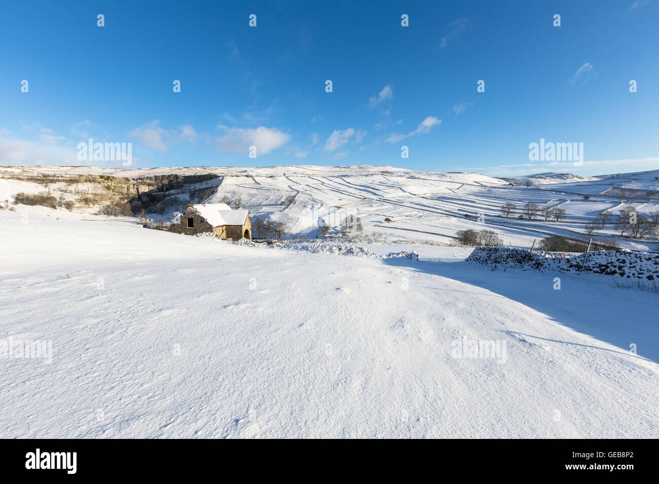 Snowy scene of traditional stone barn, fields surrounded by drystone walls and Malham Cove, Malham, Yorkshire Dales, England Stock Photo