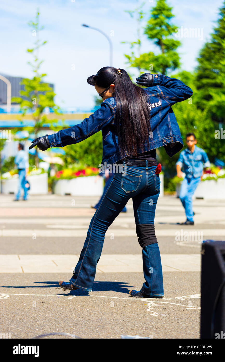Rear of female rockabilly dancer in full jean outfit and vintage hairdo dancing to rock and roll music weekly at Yoyogi park Stock Photo